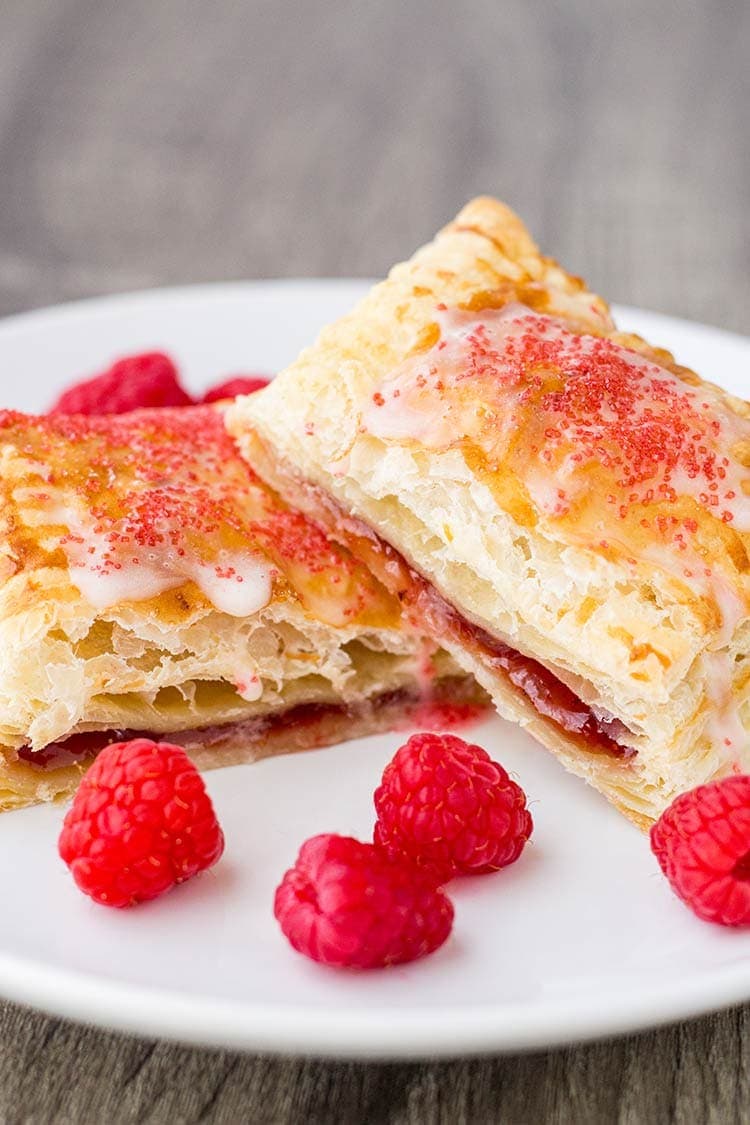 Raspberry breakfast pastry cut open on a plate, garnished with fresh raspberries.