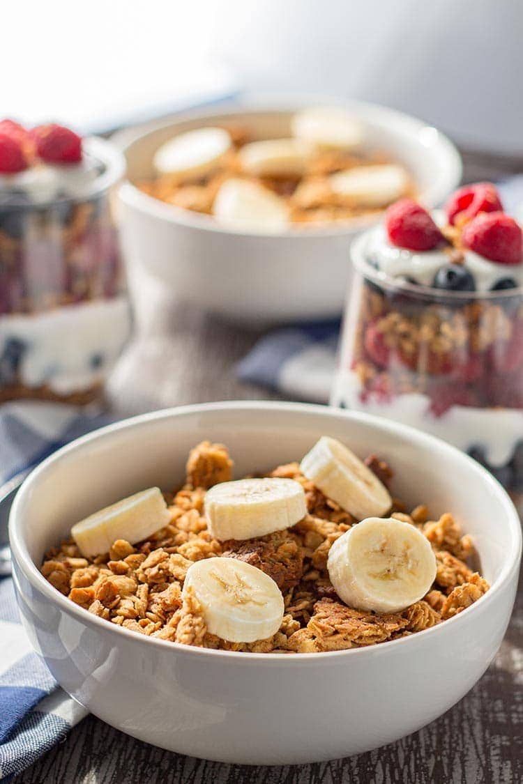 Bowls of Easy Peanut Butter Granola on table, topped with sliced bananas.