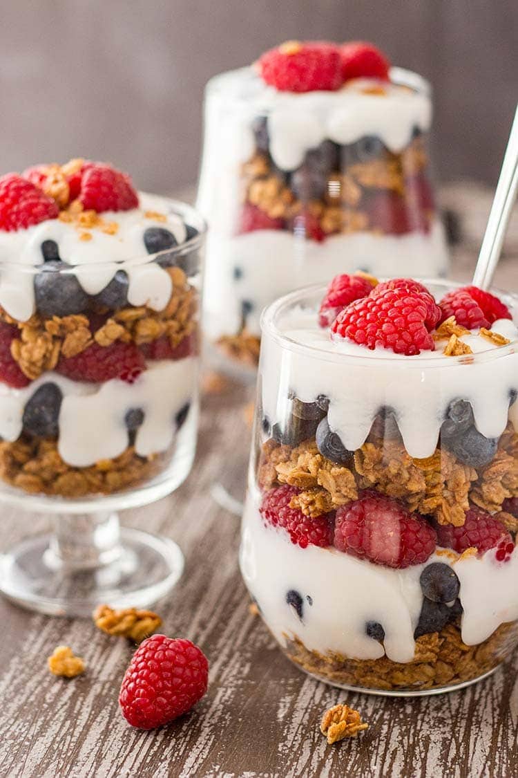 Three jars of Easy Granola Parfait garnished with raspberries, sitting on a tray.