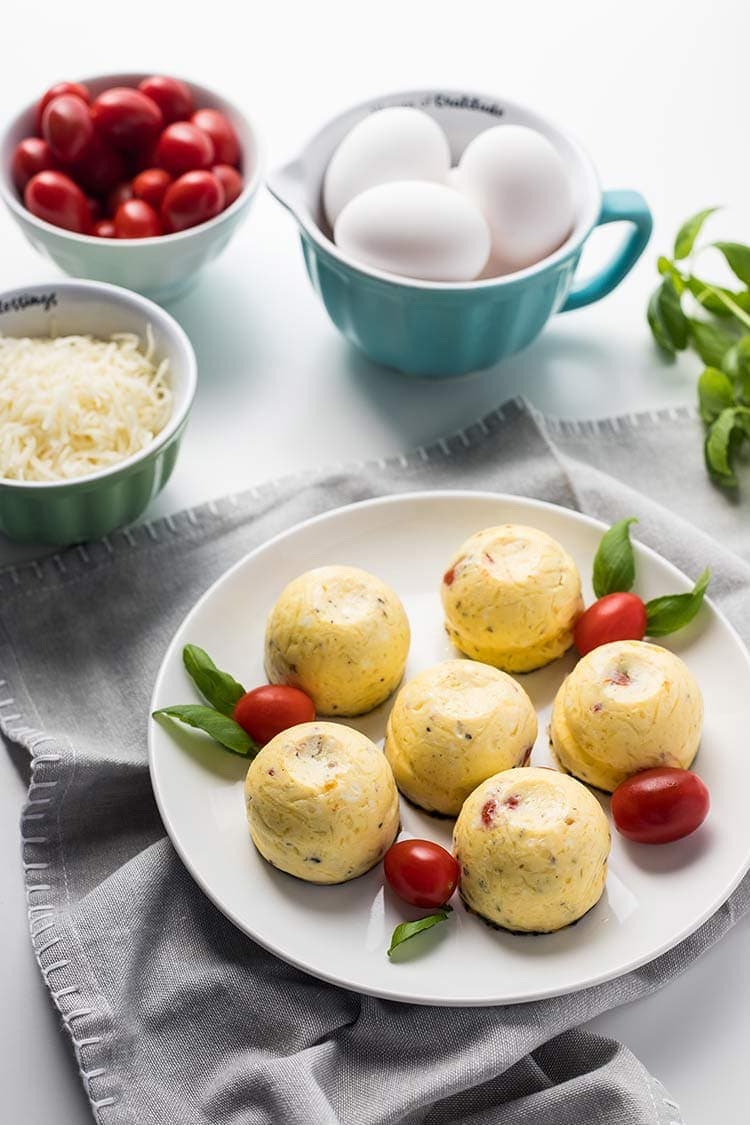 Instant Pot Caprese Egg Bites on plate next to bowls of eggs, tomatoes and shredded mozzarella cheese
