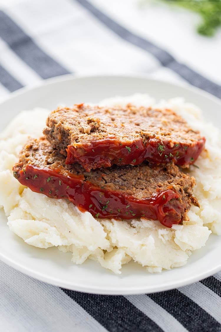 Two slices of Instant Pot Meatloaf on top of mashed potatoes and garnished with parsley.