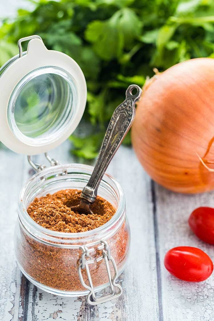 Make Your Own Taco Seasoning in a glass jar with spoon on wooden table with ingredients off to the side