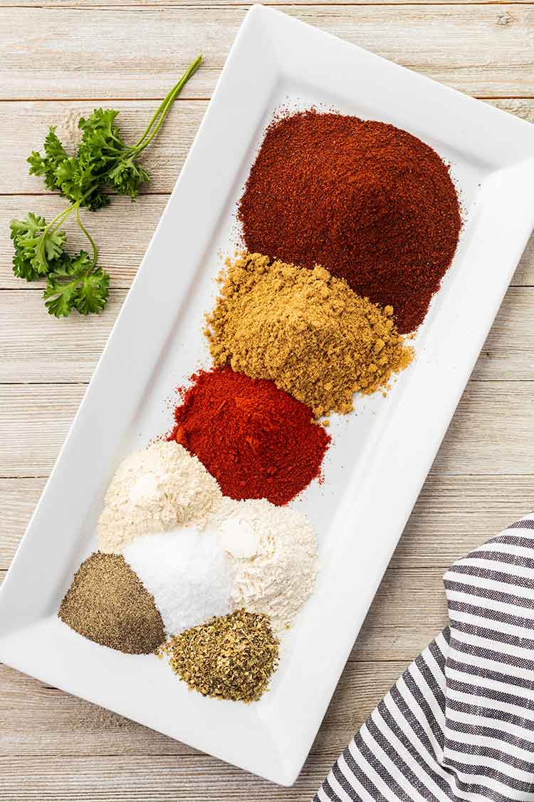 Overhead view of the various spices that are used to make Taco Seasoning Mix in piles on a small rectangular white plate