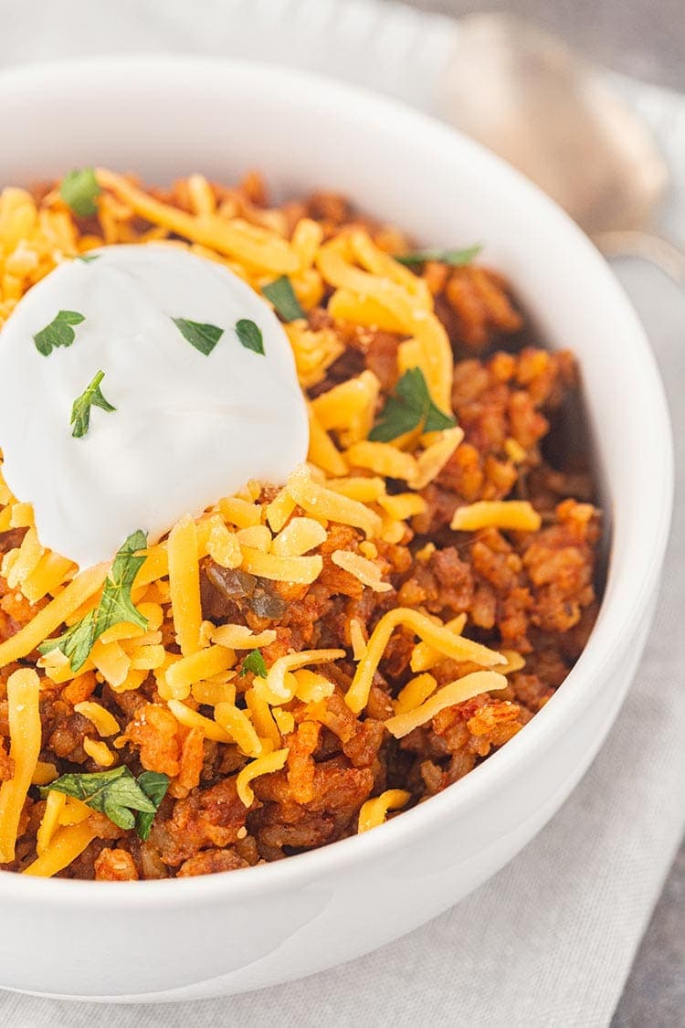 Close up shot of Beef Taco Rice Meal in a Jar in a white bowl, topped with shredded cheese and sour cream.