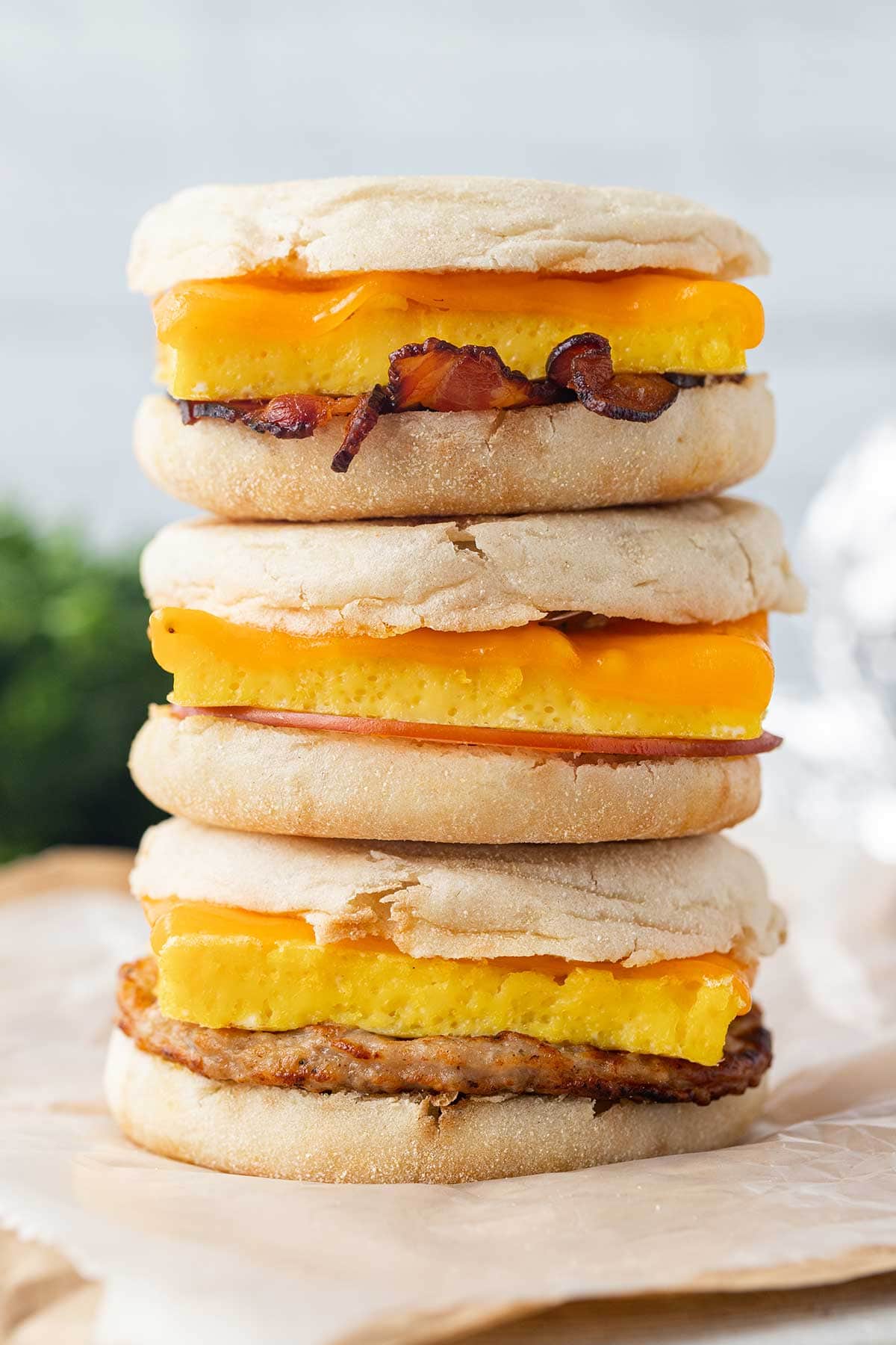 A stack of three Freezer Breakfast Sandwiches, sitting on top of sheets of parchment paper.