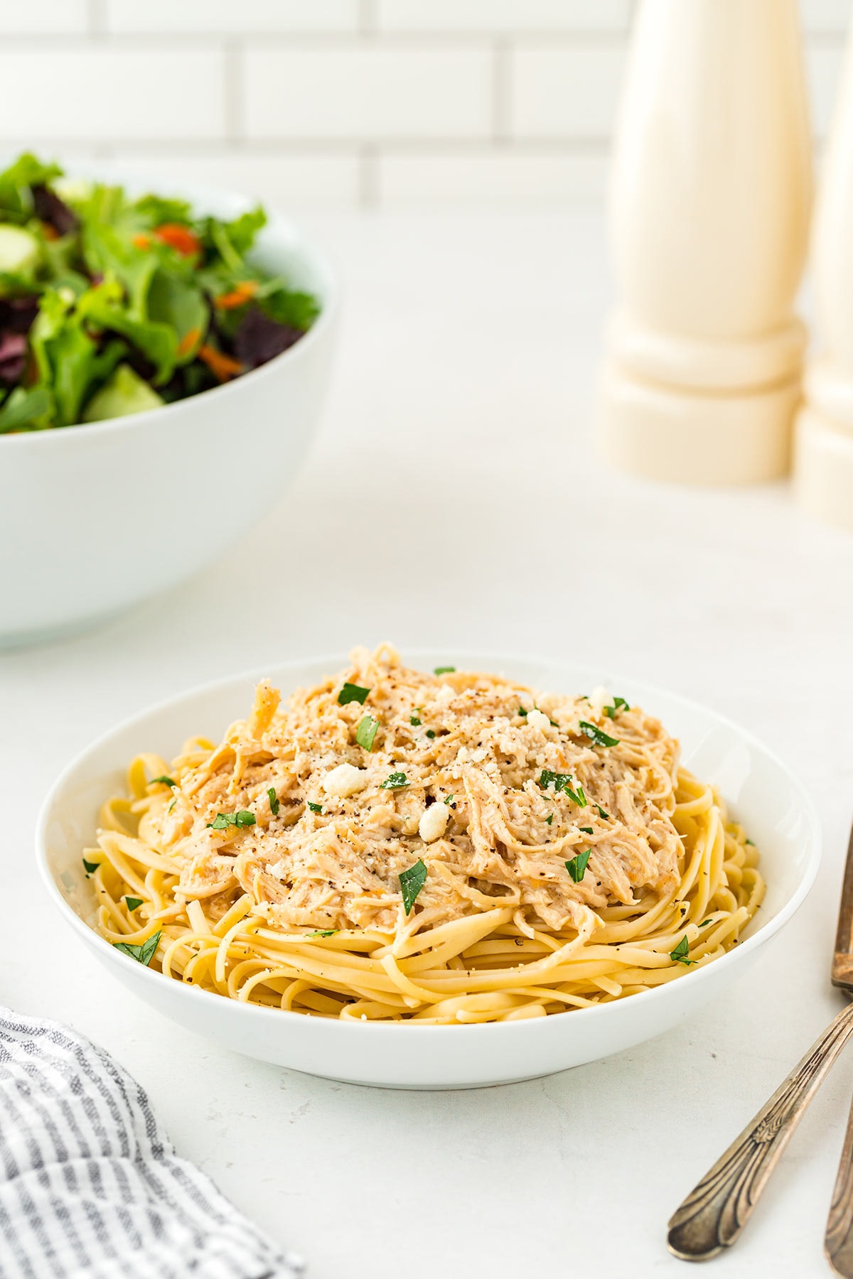 Creamy Caesar Chicken layered over cooked linguini noodles in a white dish with green parsley garnish.